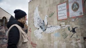 1 March 2020, Bethlehem, Palestine: A participant in the Ecumenical Accompaniment Programme in Palestine and Israel looks at the drawing of a dove carrying an olive branch while wearing a bullet proof vest and the mark of a sniper's aim, on a wall in Bethlehem.